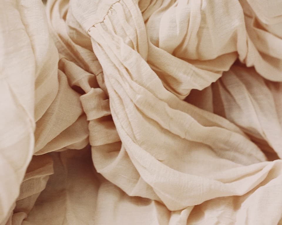 Draped lyocell material in a natural cream tone, highlighting the fluid texture and softness characteristic of TENCEL™ Lyocell fibers